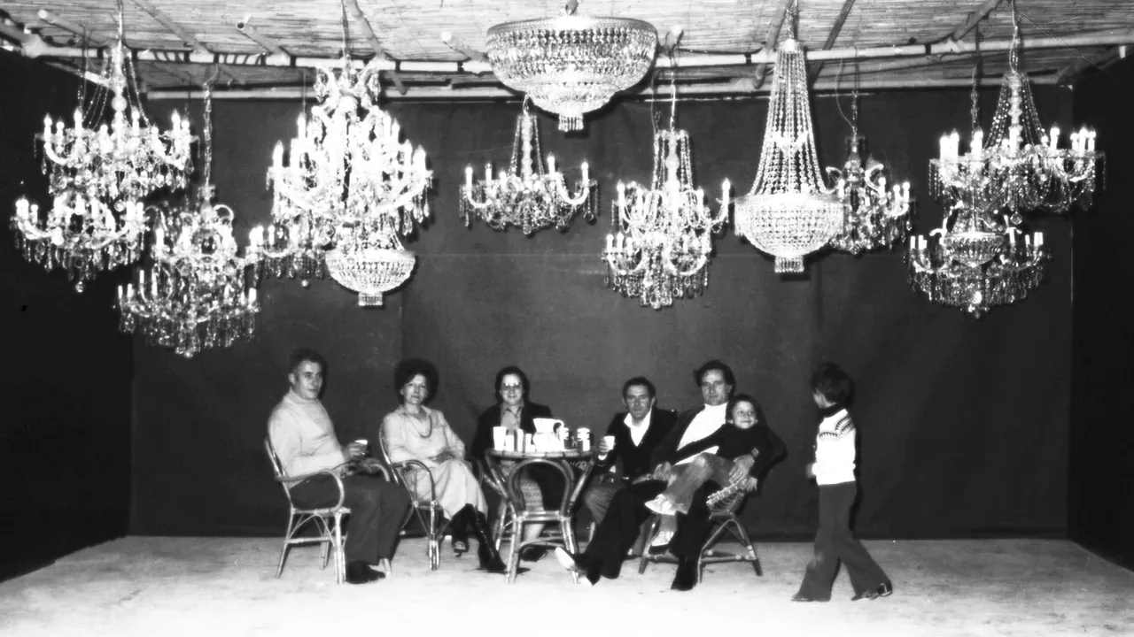 Fotografia d'archivio in bianco e nero: la famiglia fondatrice seduta sotto una fila di lampadari in cristallo.