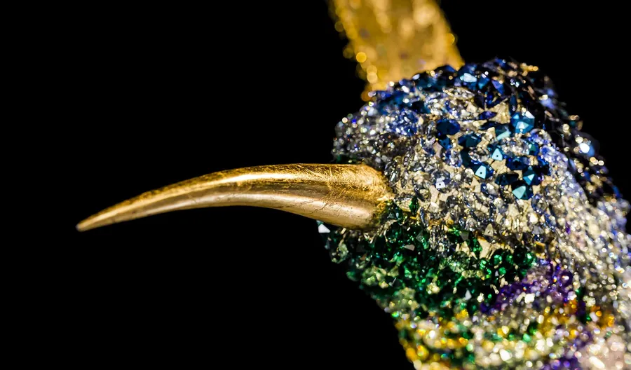 Dettaglio di un colibrì composto da cristalli policromi con becco in metallo dorato.