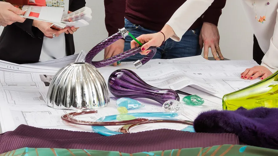Tavolo di progetto con disegni tecnici e campioni di vetro colorato.