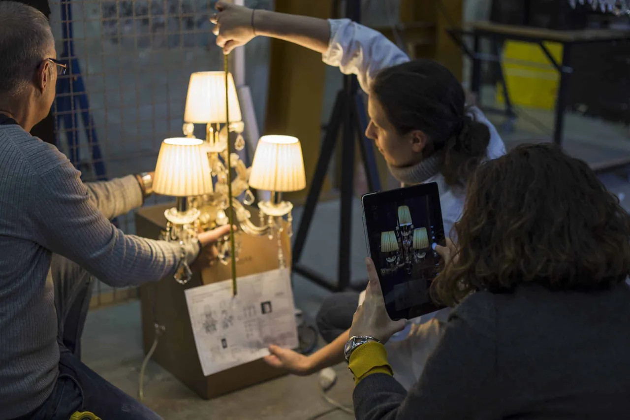 Due persone verificano un lampadario acceso confrontandolo con il disegno tecnico su tablet.