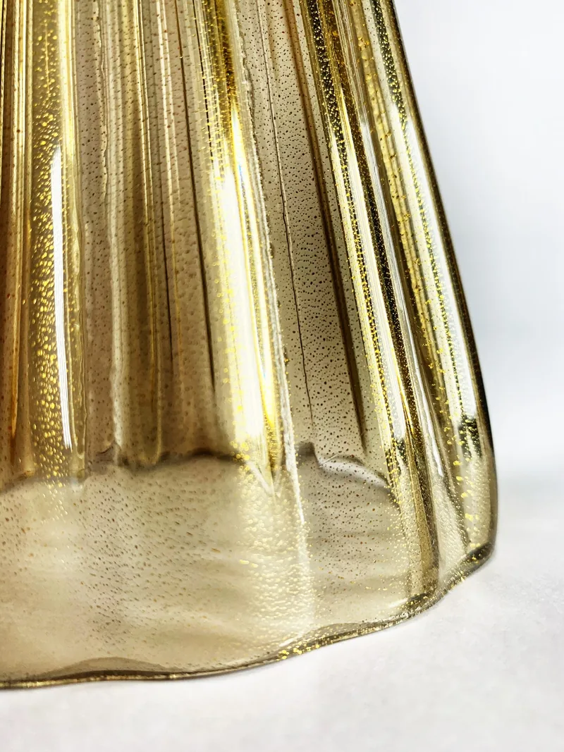 Campione di vetro soffiato fumé con foglia oro, costolato, sul fondo chiaro del tavolo.