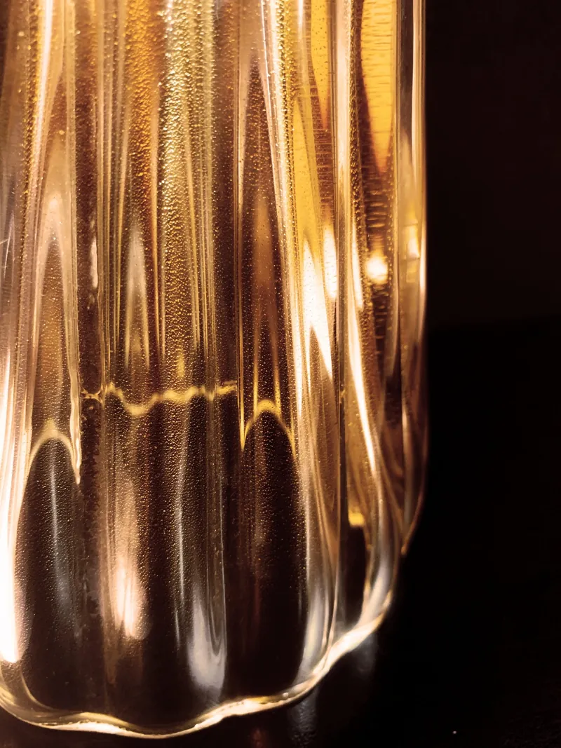 Macro di vetro soffiato in foglia oro: costolature e riflessi caldi su fondo nero.
